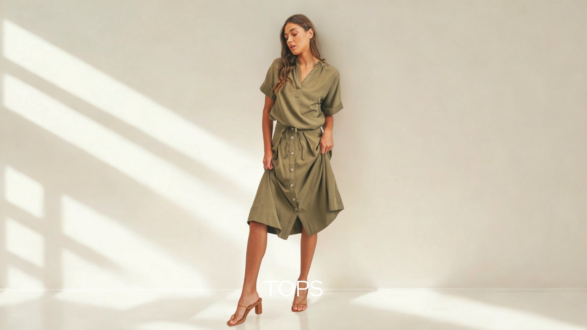 Blushe Belle Woman wearing a green dress standing in a well-lit room with shadows on the wall.